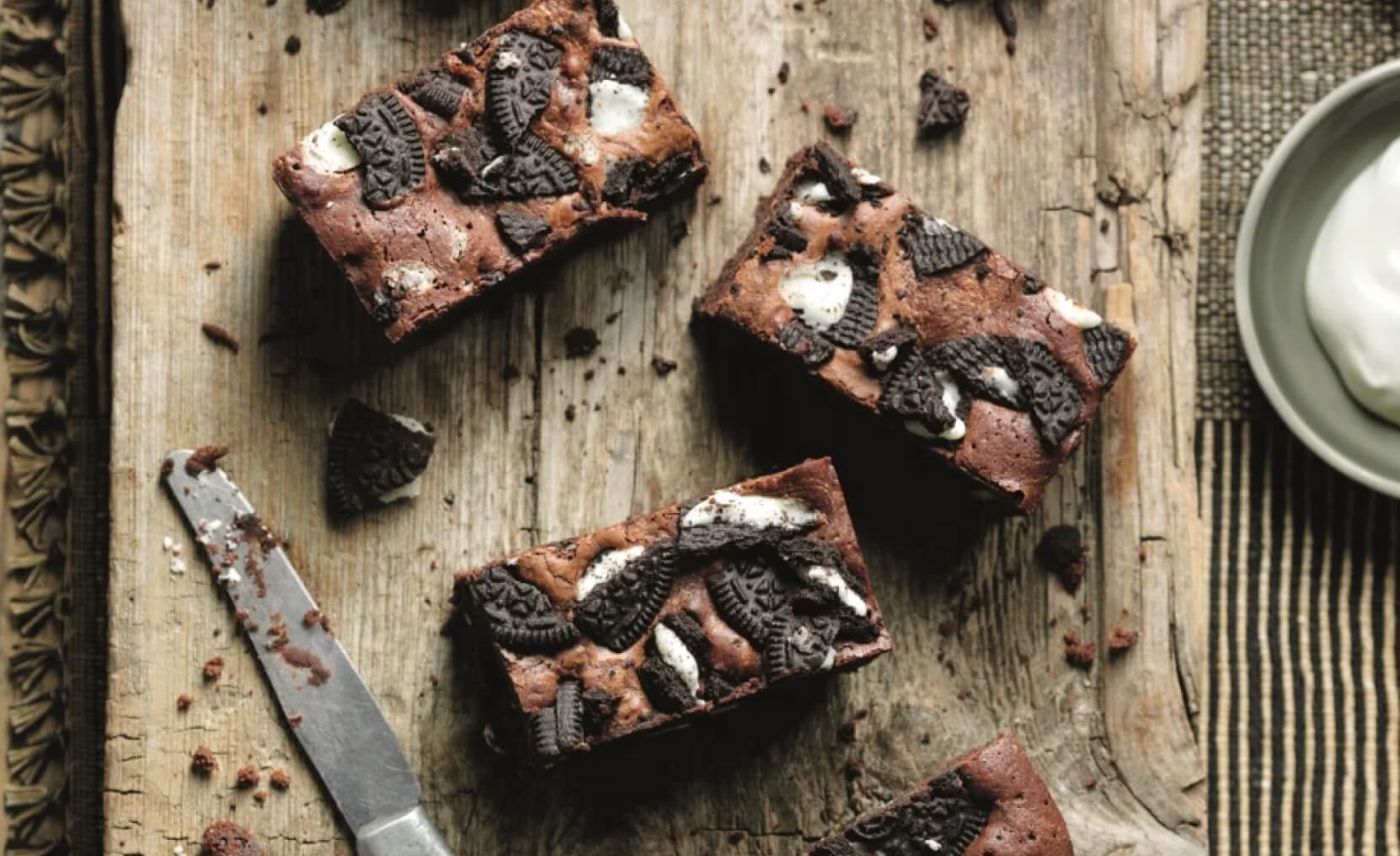 Chcoclate brownies topped with chunks of Oreo biscuits on a wooden chopping board.